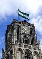 Photographie en couleurs d'un clocher d'église et de son drapeau municipal.