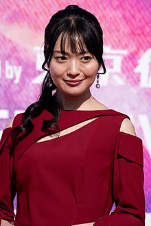 waist up portrait of Kitahara in dark red dress, facing to right of audience