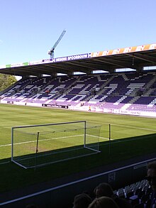 Photographie montrant un but, le terrain et une tribune du stade avec l'inscription « BEERSCHOT » sur les sièges.