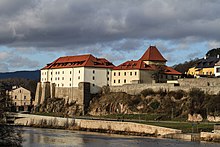 Fotografie hradu stojícího nad řekou. Hrad má jednu nízkou masivní věž zastřešenou valbovou střechou.