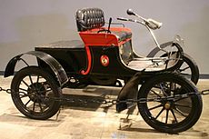 Olds Curved Dash 6C 1904. Este modelo, presentado en 1901 polo industrial Ransom Eli Olds, é considerado o primeiro en ser producido en serie e o primeiro en inaugurar o sistema de cadea de montaxe.