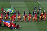 Deux équipes (en rouge et en jaune) entrent sur un terrain de football, accompagnés d'enfants
