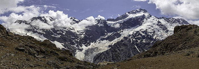 Une grande montagne enneigée caressée de quelques nuages. Un glacier en descend.