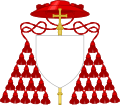 External ornaments of a cardinal's coat of arms, incorporating a scarlet galero with fifteen scarlet tassels on each side and a patriarchal cross behind the escutcheon and the motto