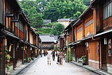 Rue dont les deux trottoirs sont surplombés par des maisons en bois à un étage.