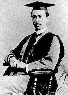 Photographie en noir et blanc d'un jeune homme assis dans une attitude digne, arborant le mortarboard académique de la remise des diplômes dans les pays anglo-saxons.