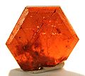 Hexagonal-tafeliger, rötlich durchscheinender Bastnäsit-(Ce)-Kristall aus dem gleichen Fundort (Größe: 1,5 × 1,5 × 0,3 cm)