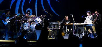 Dylan together with five members of his band onstage. Dylan, dressed in a white shirt and black pants, is second from right.