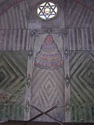 Camide bulunan Davud'un Yıldızı desenli yuvarlık bir vitray, mihrab ve rahle.