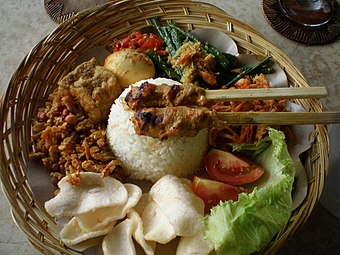 وعده شخصی نازی بالی، بشقاب بامبو بافته شده با برنج که توسط تکه‌های غذاهای جانبی گوشت و سبزیجات احاطه شده‌است.