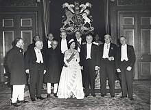 Élisabeth II en robe du soir et portant une tiare est entourée de onze hommes en tenue de soirée ou en costume national.