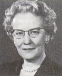 Cecilia H. Hauge, a smiling middle-aged white woman with short curly grey hair, wearing cat-eye glasses and a strand of pearls