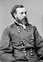 Black and white photo shows a man with dark hair and a beard. He wears a dark military uniform with the shoulder tabs of a major general (two stars).