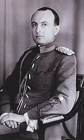 Photographie en noir et blanc montrant un homme assis, de trois-quart, portant un uniforme militaire.