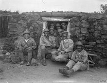Desítka usmívajících se italských vojáků sedících v zákopu.