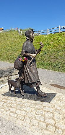 Sebuah patung perunggu berjalan dari Mary Anning dengan beliung dan fosil di tangannya. Seekor anjing berjalan di sampingnya