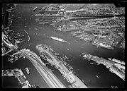 Luchtfoto van het IJ en omgeving, gezien in noordwestelijke richting. Op de voorgrond de Dijksgracht met de Piet Heinkade en de Oostelijke Handelskade. Rechts de IJhaven met de Javakade. Rechtsmidden de scheepswerf van de ADM. Daarachter de Meeuwenlaan en Vogelbuurt in Amsterdam-Noord. Midden boven de Willemssluizen in het Noordhollandsch Kanaal. Linksboven de De Ruijterkade; circa 1930. Luchtvaartafdeeling, 1920-1940.