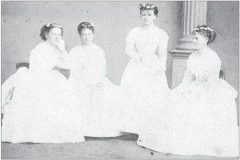 A black and white photograph of four young white women wearing white dresses.