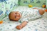 A smiling baby lying in a soft cot