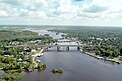 Das Schrägluftbild zeigt einen Fluss, den eine große und zwei kleinere Brücken überspannen; links und rechts des Flusses ausgedehnte Waldgebiete und einzelne Straßenzüge mit Häusern