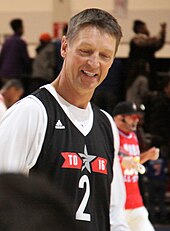 A middle-aged man wearing a white long-sleeved shirt underneath a black basketball tank top.