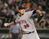 A man in a grey pinstriped baseball uniform throws a baseball with his right hand. The uniform reads "Minnesota" across the chest (partially obscured) in red letters, below which is the number "36", also in red. He is wearing a navy blue baseball cap with a lower-case red "m" on the front. The man is looking toward the right side of the image.