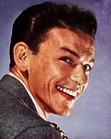 Close-up studio photograph of a young, smiling Sinatra with styled hair wearing a suit and tie