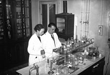 Photo en noir et blanc. Un couple de chimistes en blouse blanche dans leur laboratoire.