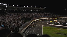 A photo of NASCAR cars racing at the 2008 Bank of American 500 during night time.
