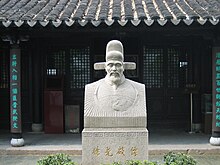 A bust of Xú Guāngqǐ sits in the middle of a courtyard, surrounded by bushes and a roof.