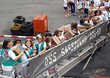 Girl Scouts and Brownies from two troops in Singapore pass Girl Scout cookie boxes up the brow of the rescue and salvage ship USS Safeguard (ARS 50) as part of Operation Thin Mint.