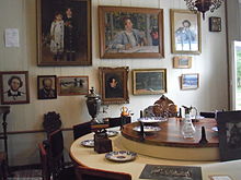 Photographie d'un intérieur bourgeois, des tableaux sont accrochés aux murs.