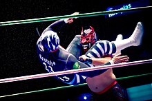 An action shot of La Sombra with his legs wrapped around Mephisto's head, flipping to throw him to the ground.