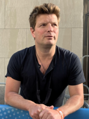 Harvey resting his arms in a fence at the backstage, wearing a black shirt