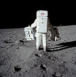 Un homme en combinaison spatiale sur la Lune, transportant deux objets.