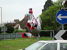 The sculpture, viewed from the front, wearing ornate red and blue knitwear on the head and drooping around the neck