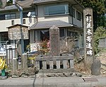 A stone stele with square cross section surrounded by a stone fence.