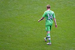 A colour photograph of Kevin de Bruyne, face back to the camera, wearing an all-green kit.