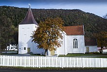 Foto einer weißen Holzkirche, im Hintergrund eine Erhebung