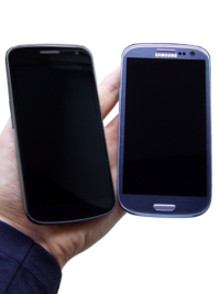 Photo of two phones turned off held next to each other with warm yellow ambience lightning. The phones are rested on a person's hand.