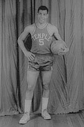 A man, wearing a jersey with a word "TEMPLE" and the number "5" written in the front, is holding a basketball while posing for a photo