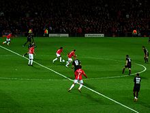 A wide shot of a football match with Manchester United in red in possession against Lyon in black.