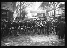 Photographie en noir et blanc de coureurs cyclistes sur une place.
