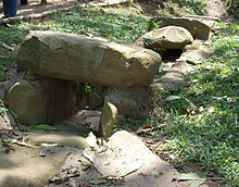 A stone-lined channel set into a grassy embankment. The sides of the channel are formed by upright stones and parts of the channel are covered with capstones.