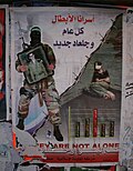 Affiche sur le mur d'une maison en « Cisjordanie » (ou « Judée-Samarie »). Un « combattant » (ou « terroriste ») du Hamas brandit une photo du « prisonnier » (ou de l'« otage ») Guilad Shalit en comparant son sort à celui des « prisonniers » (ou « terroristes ») palestiniens détenus en Israël.