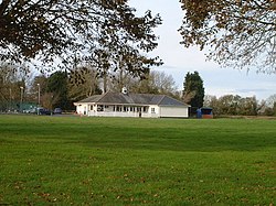 White building with grey roof in the middle of green grass area.