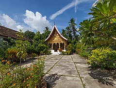 Vat Pa Phai temple in its garden with orange marigold, clouds and blue sky, in Luang Prabang.jpg