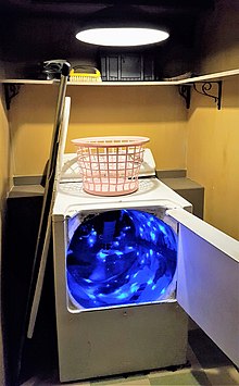 A clothes dryer in a utility closet. Inside the machine's tub, a blue light illuminates the beginning of a tunnel