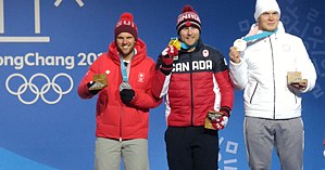 Three men standing on a podium holding up the medals that they won in the men's ski cross event.