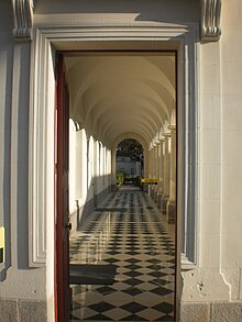 Galerie de pierre blanche, le plafond est voûté, le carrelage brillant est en damier noir et blanc.